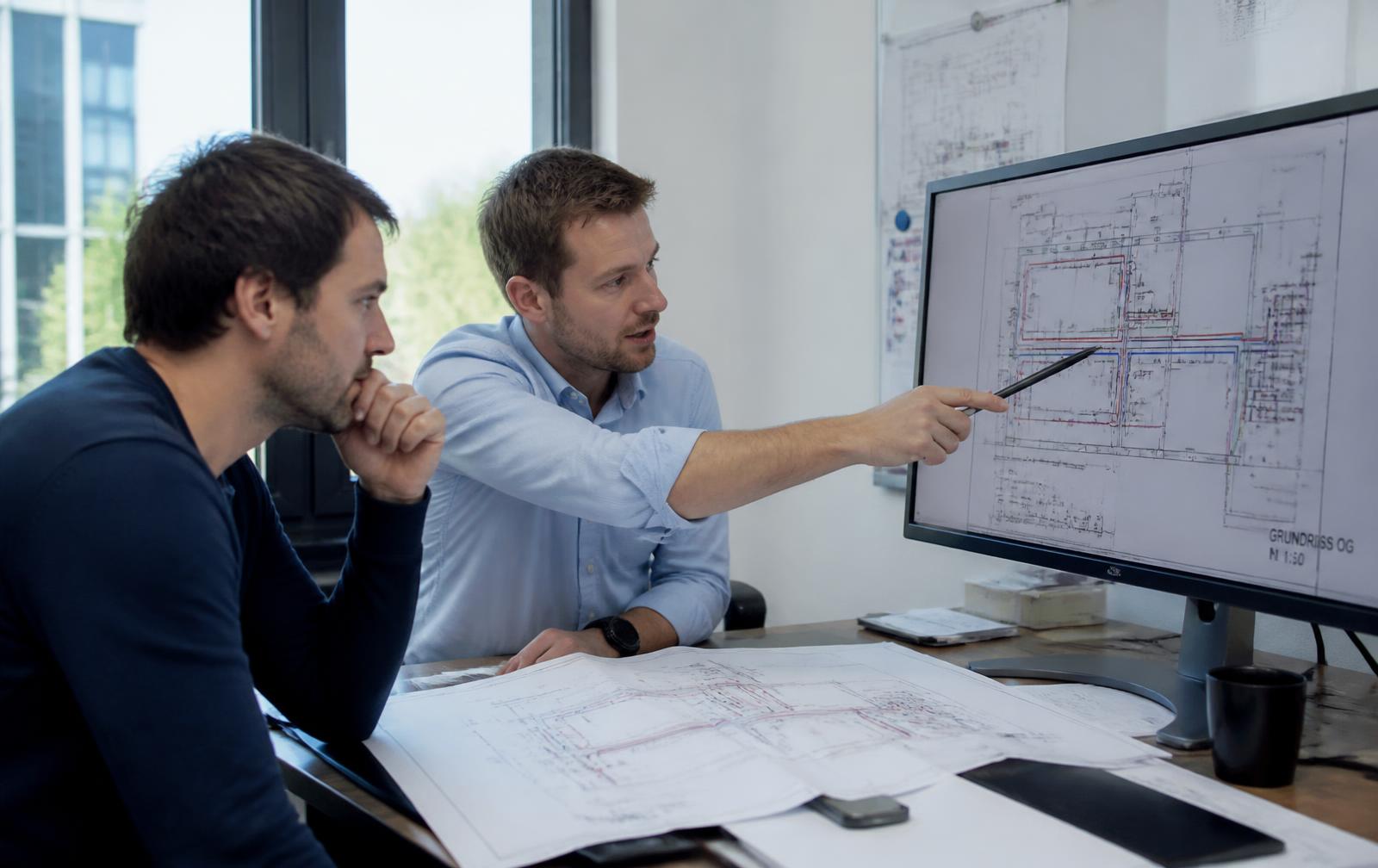 Zwei TGA-Fachplaner besprechen Grundrisse und Schemata im Büro